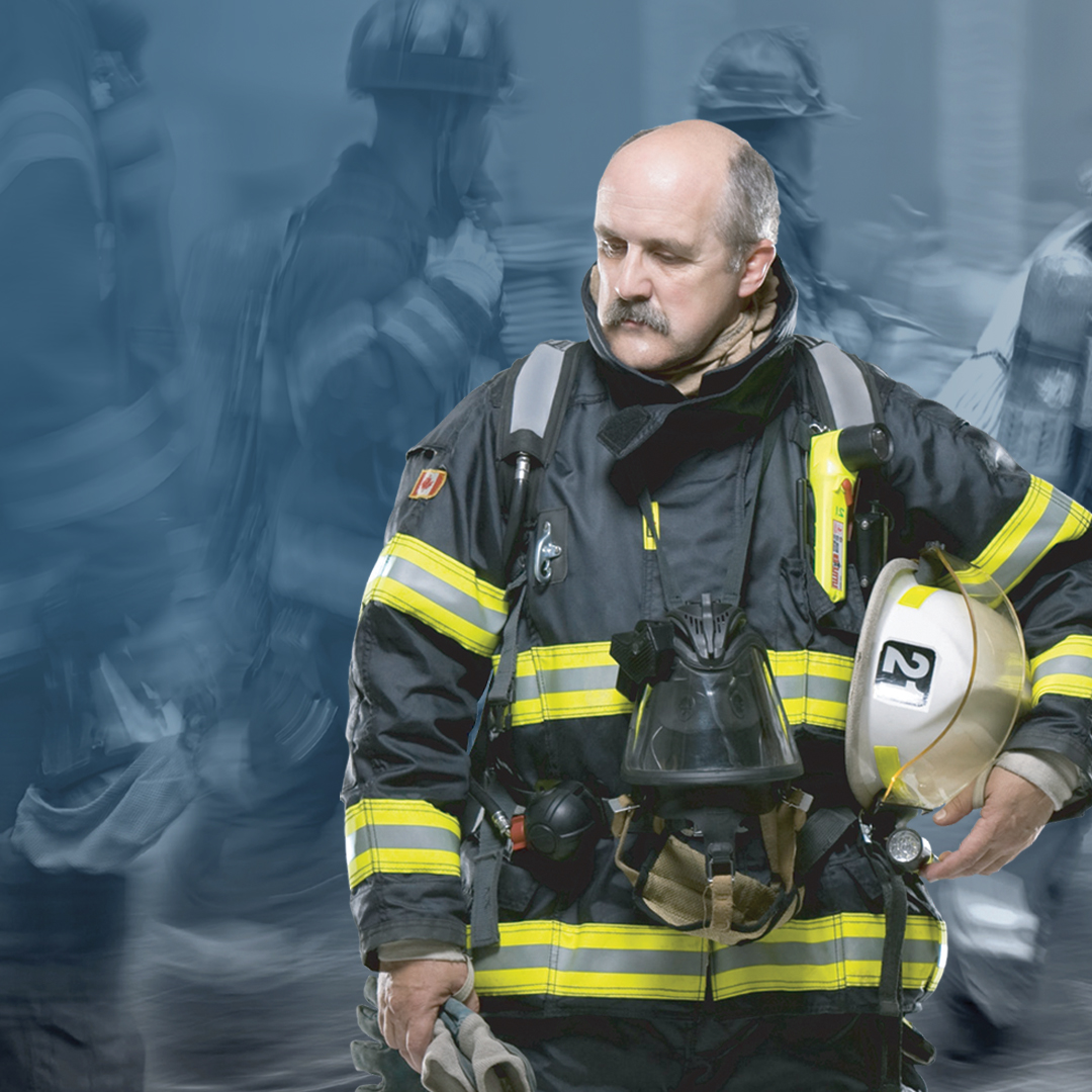 Firefighter in gear holding helmet amid blurred crew